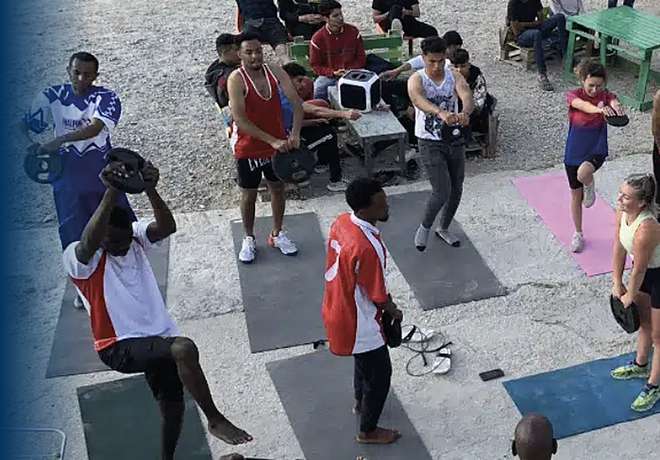 Adults and children exercising together outdoors on mats