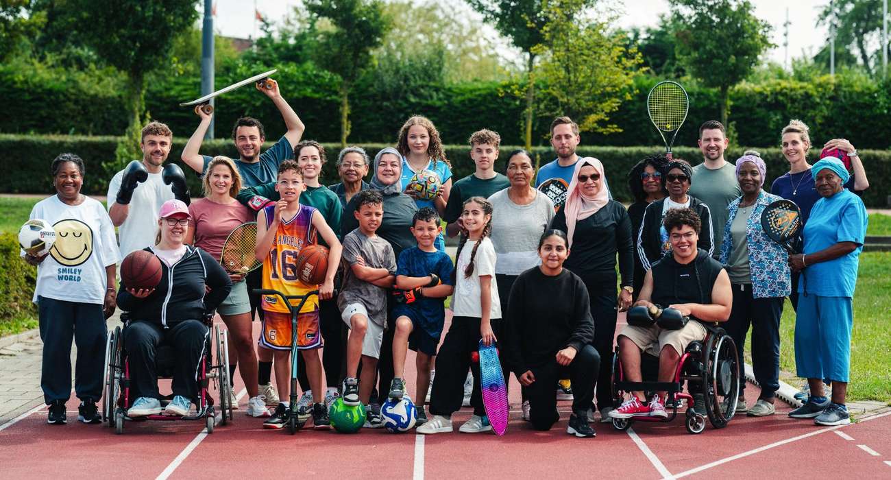 A community group of all ages, including wheelchair users, holding equipment from many different sports