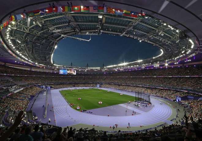 An international stadium at night ringed by the flags of many nations
